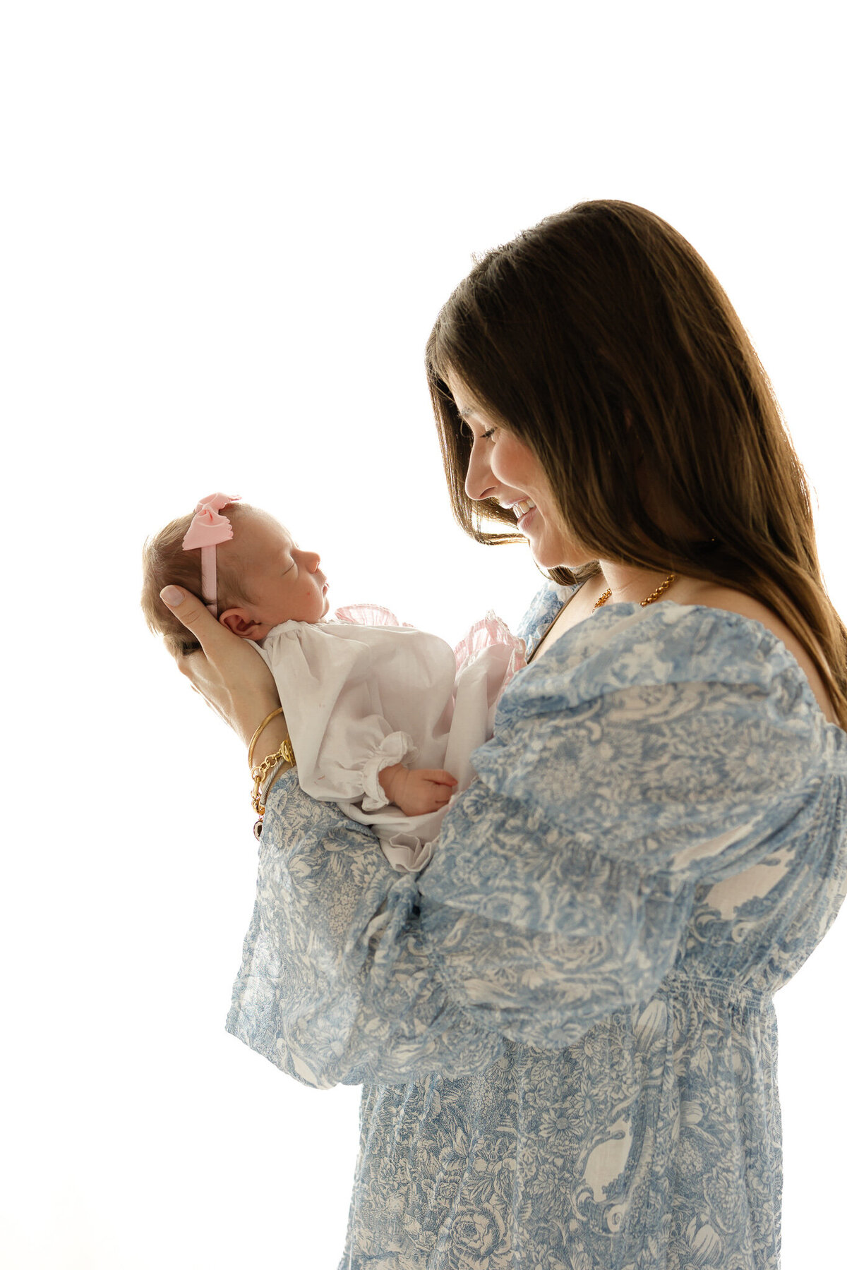 Young mom wearing a blue toile dress holding her newborn girl smiling at her