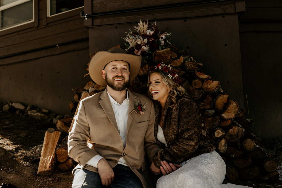 Bride and groom sitting together in front of a pile of logs