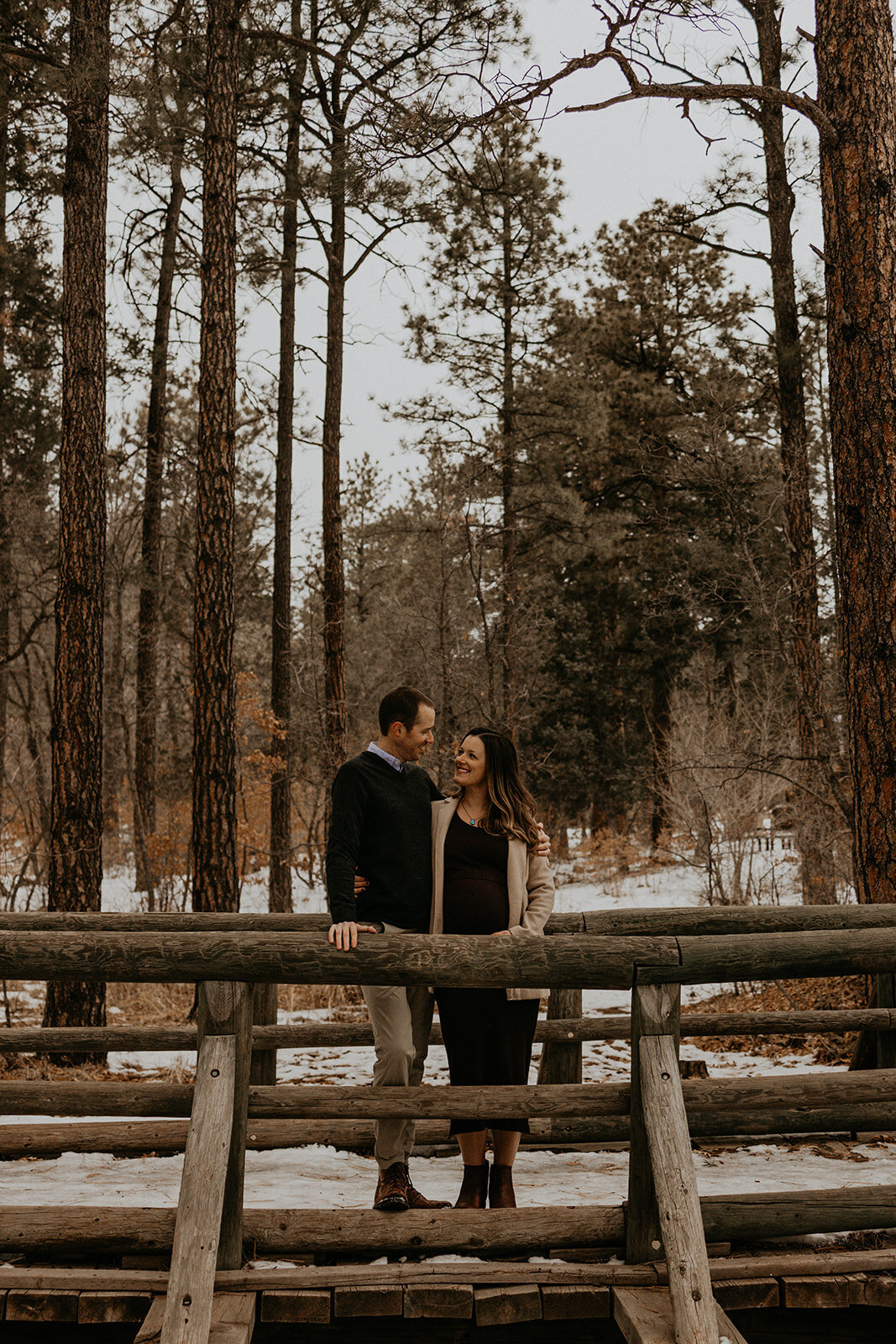 expecting couple standing on a walking bridge in the forest