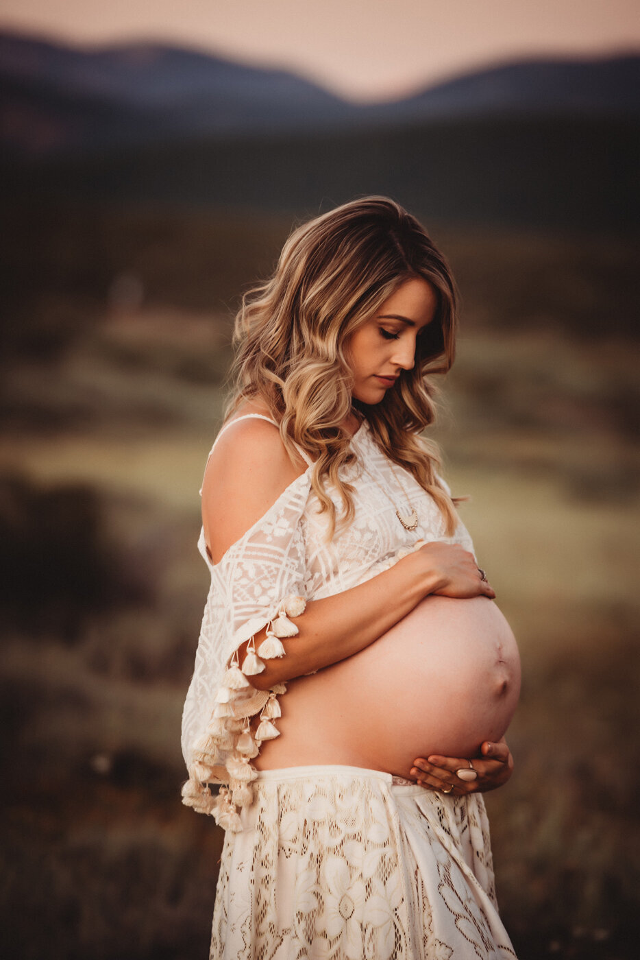 Stunning pregnant mama wearing a cream gown while cradling and looking down at her belly