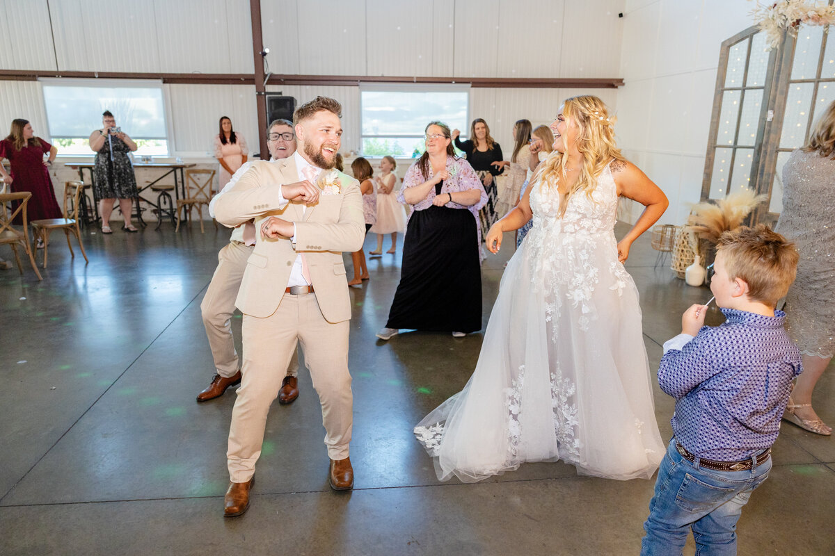 The bride, groom, and guests dance energetically at the wedding reception, celebrating with smiles and fun moves.