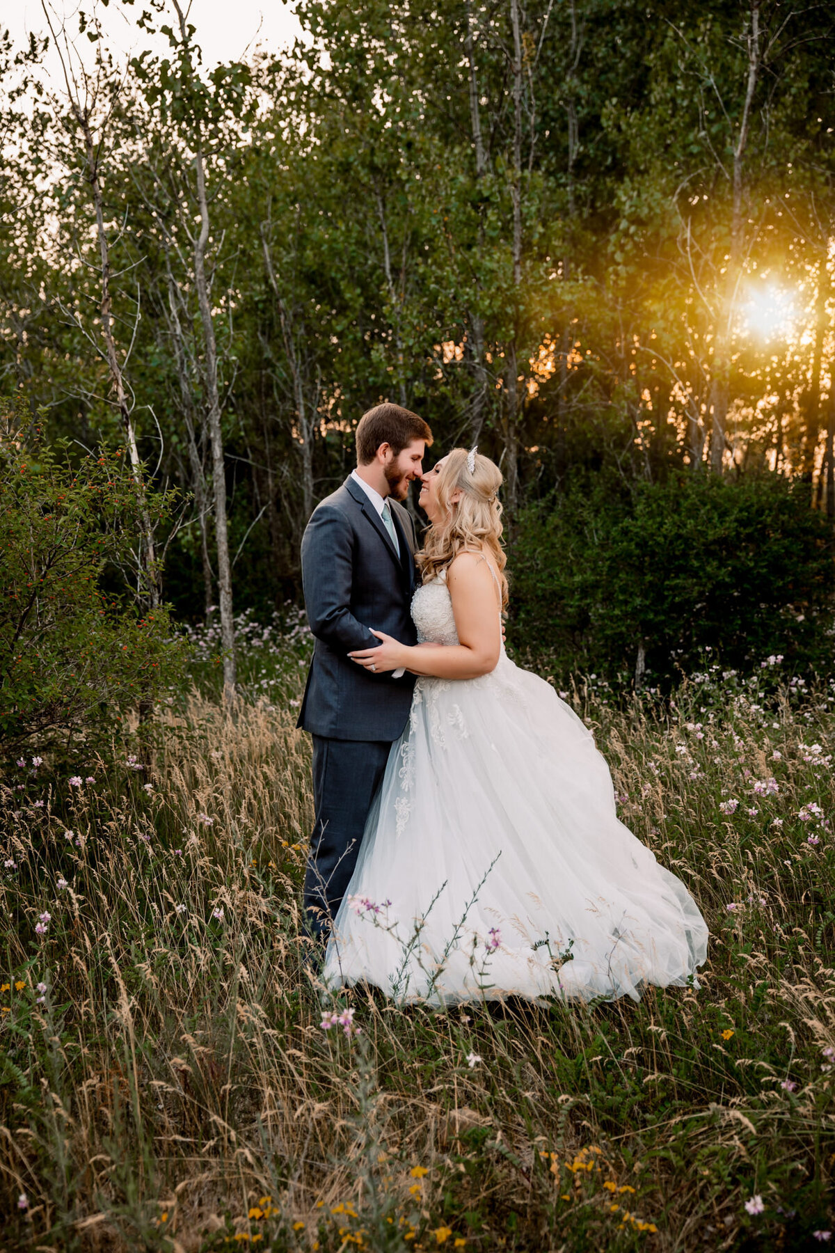 bride and groom stand in field at sunset