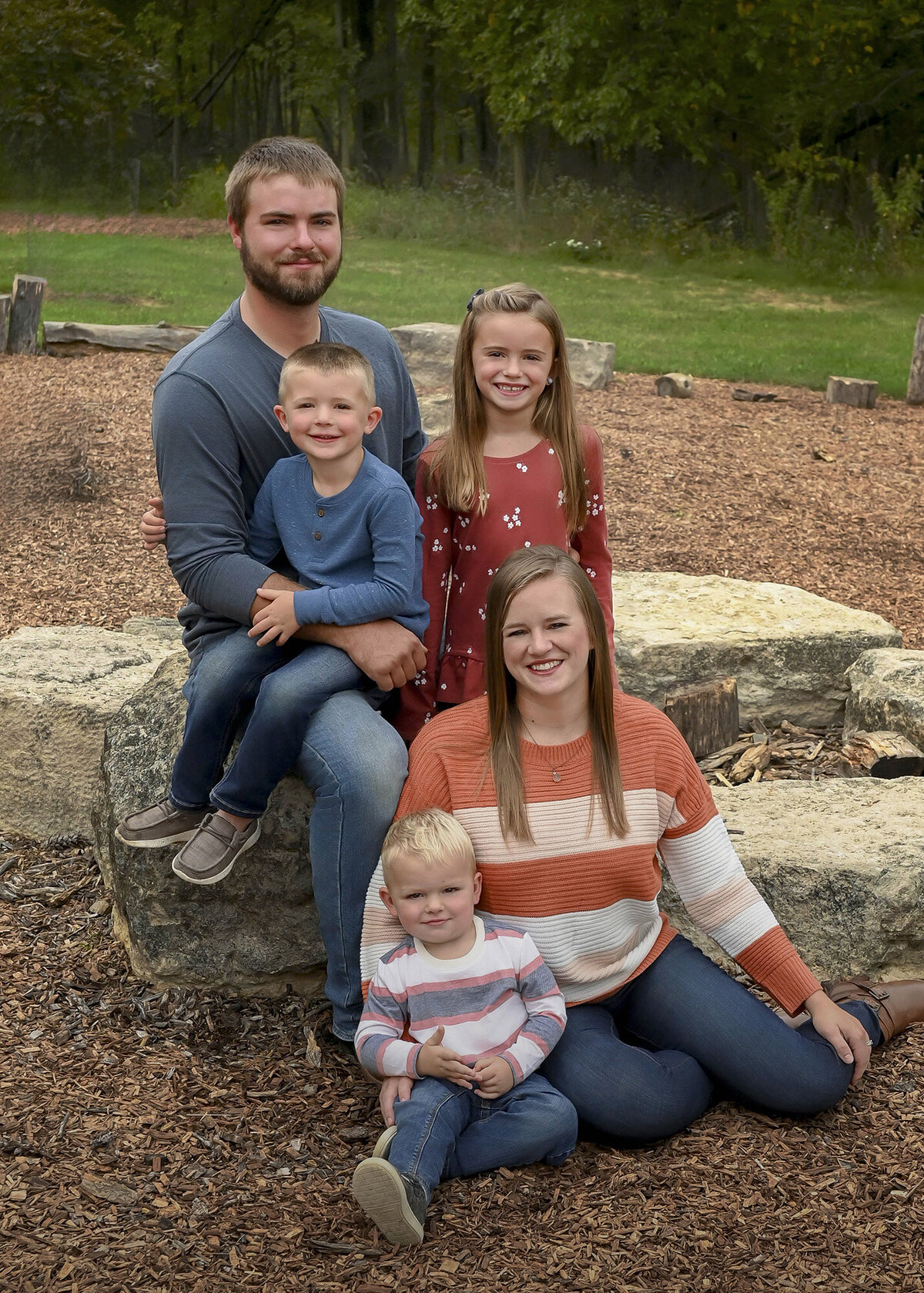 Parents and 3 children sitting together on rocks in a park-like setting