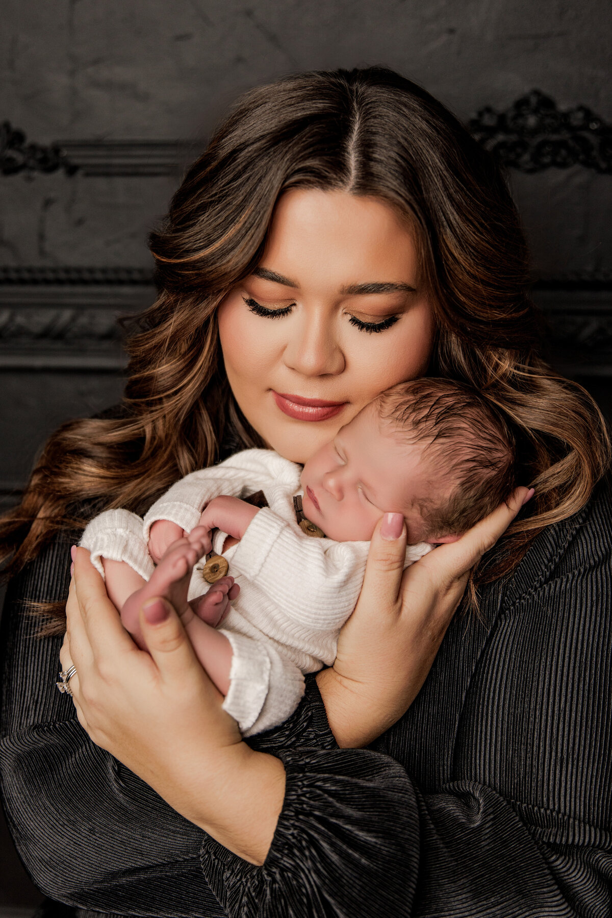 mother holding newborn son with a black backdrop