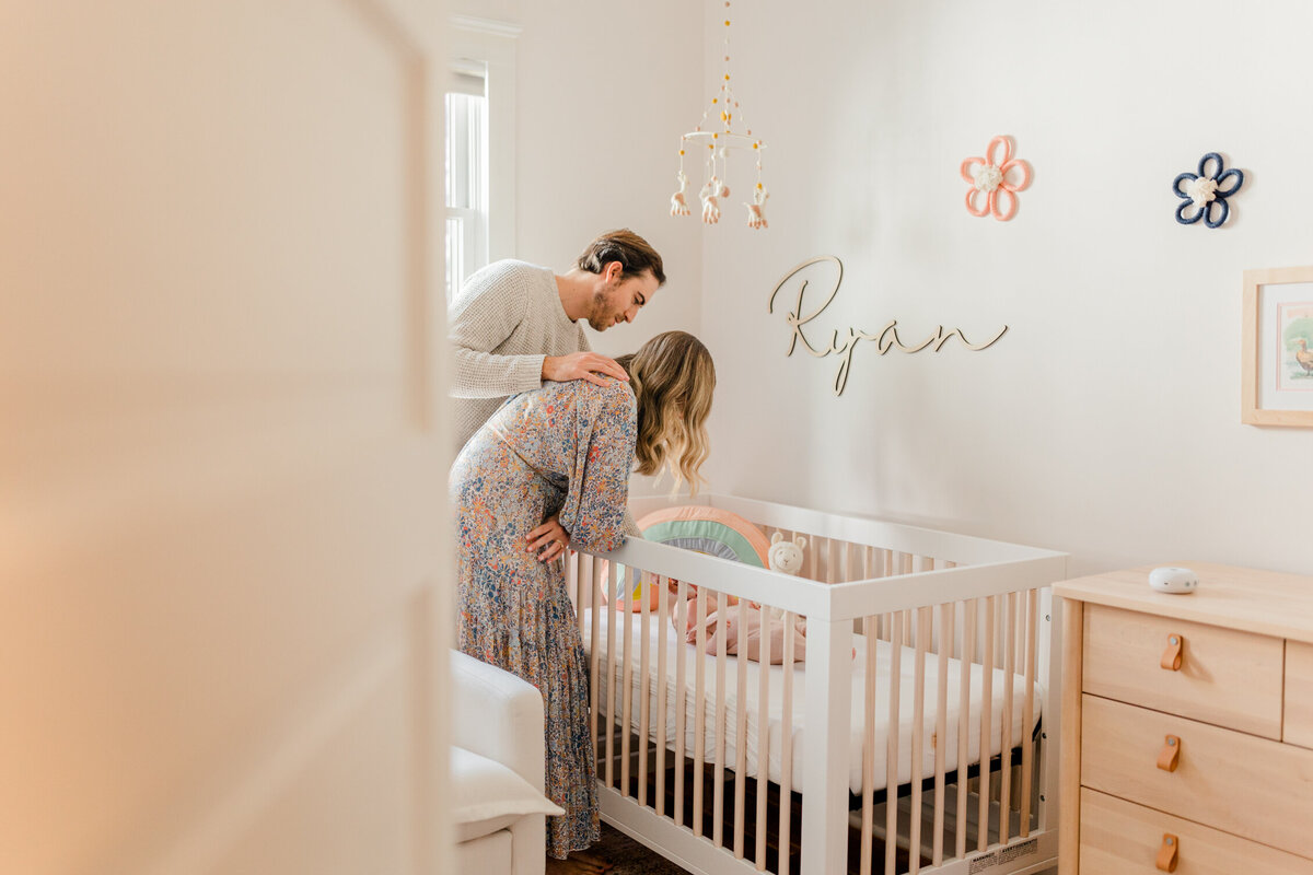 Wide view of the door leading into a newborn's nursery, showing mother and father standing together over the newborn's crib