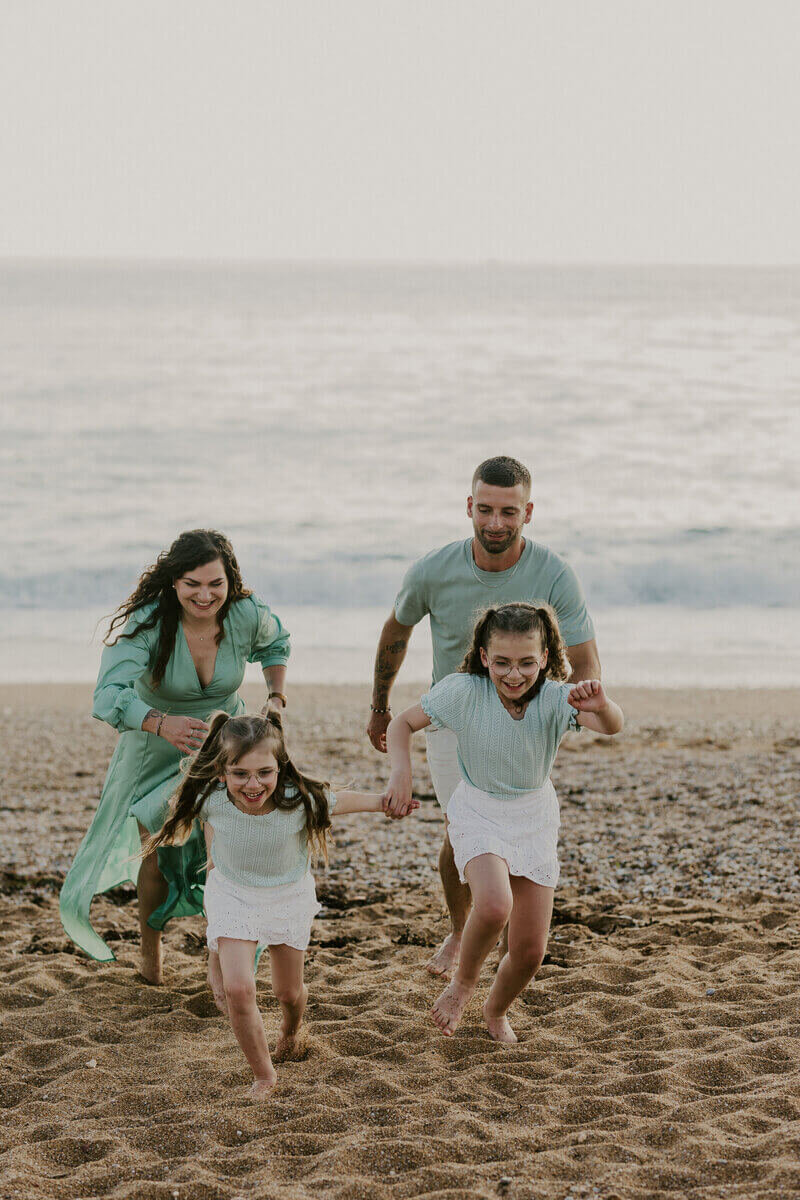 Deux parents courant derrière leurs deux petites filles à la plage, tous habillés en vert et blanc. Photo prise par Laura, photographe famille en vendée.