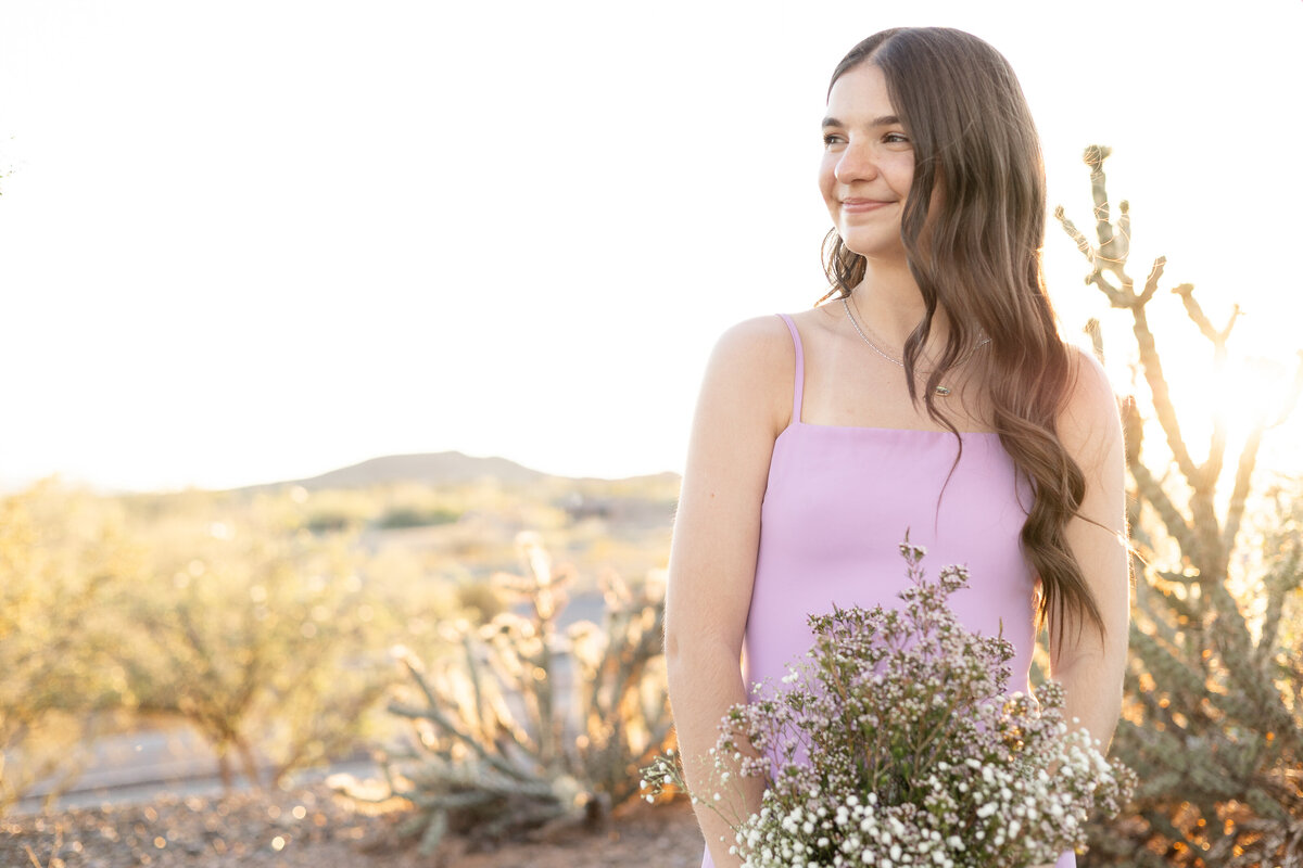 Senior girl holds floral bouquet and smiles during sunset in Vistancia neighborhood in Peoria, Arizona.