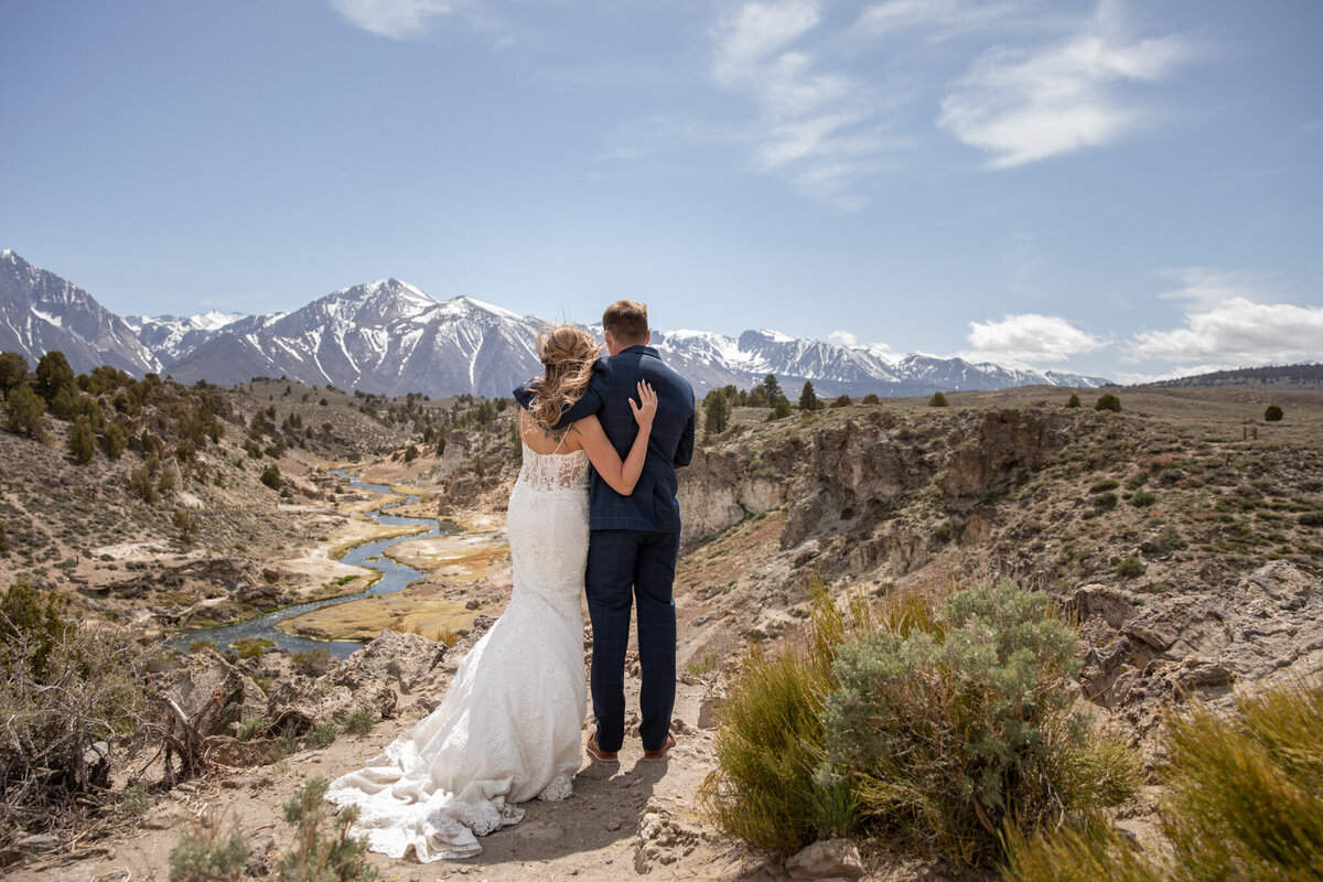A bride and groom stand looking at the mountain views while their California elopement photographer takes their pictures.