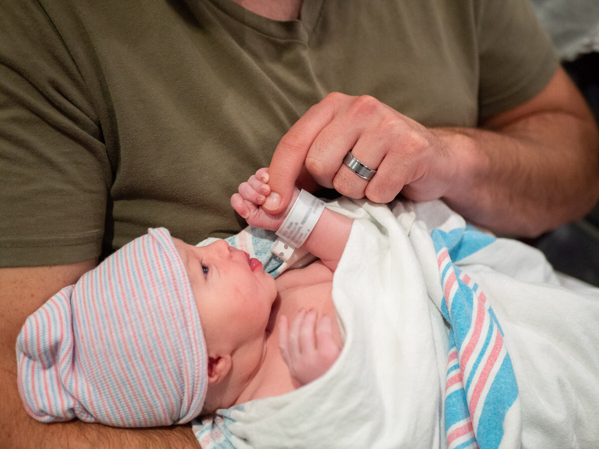 A new dad is holding his newborn at a hospital in Seattle. The baby's tiny hand is holding on of the dad's fingers.