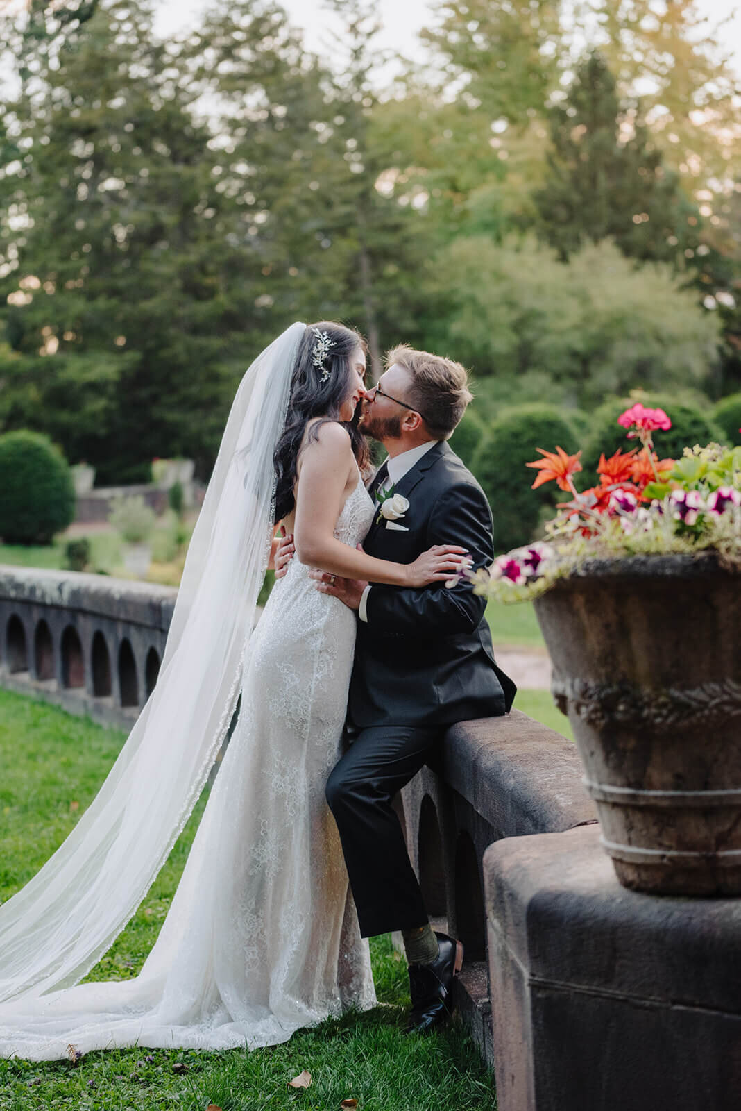 Groom sitting on stone wall kissing bride at Finger Lakes wedding, NY