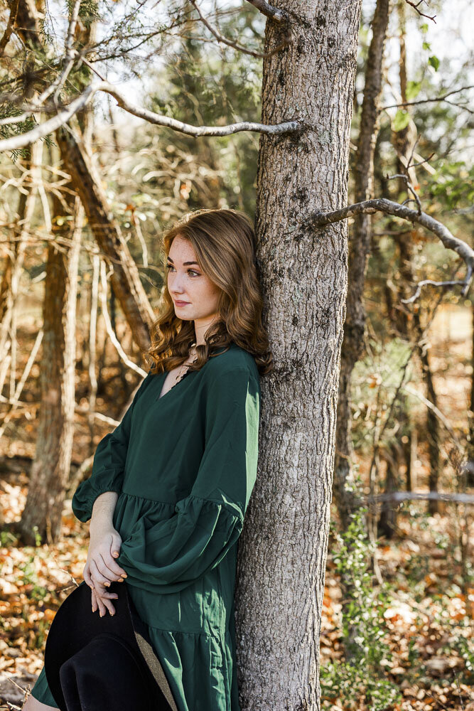 Girl thoughtfully posing while leaning her back agasinst a pine tree