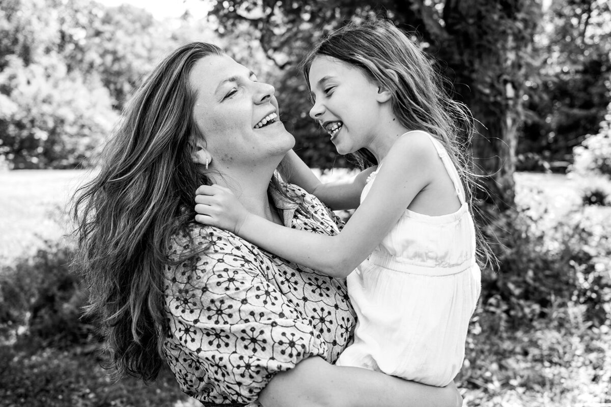 Candid black and white photo of a mother and daughter laughing together outdoors, taken by a Connecticut family photographer