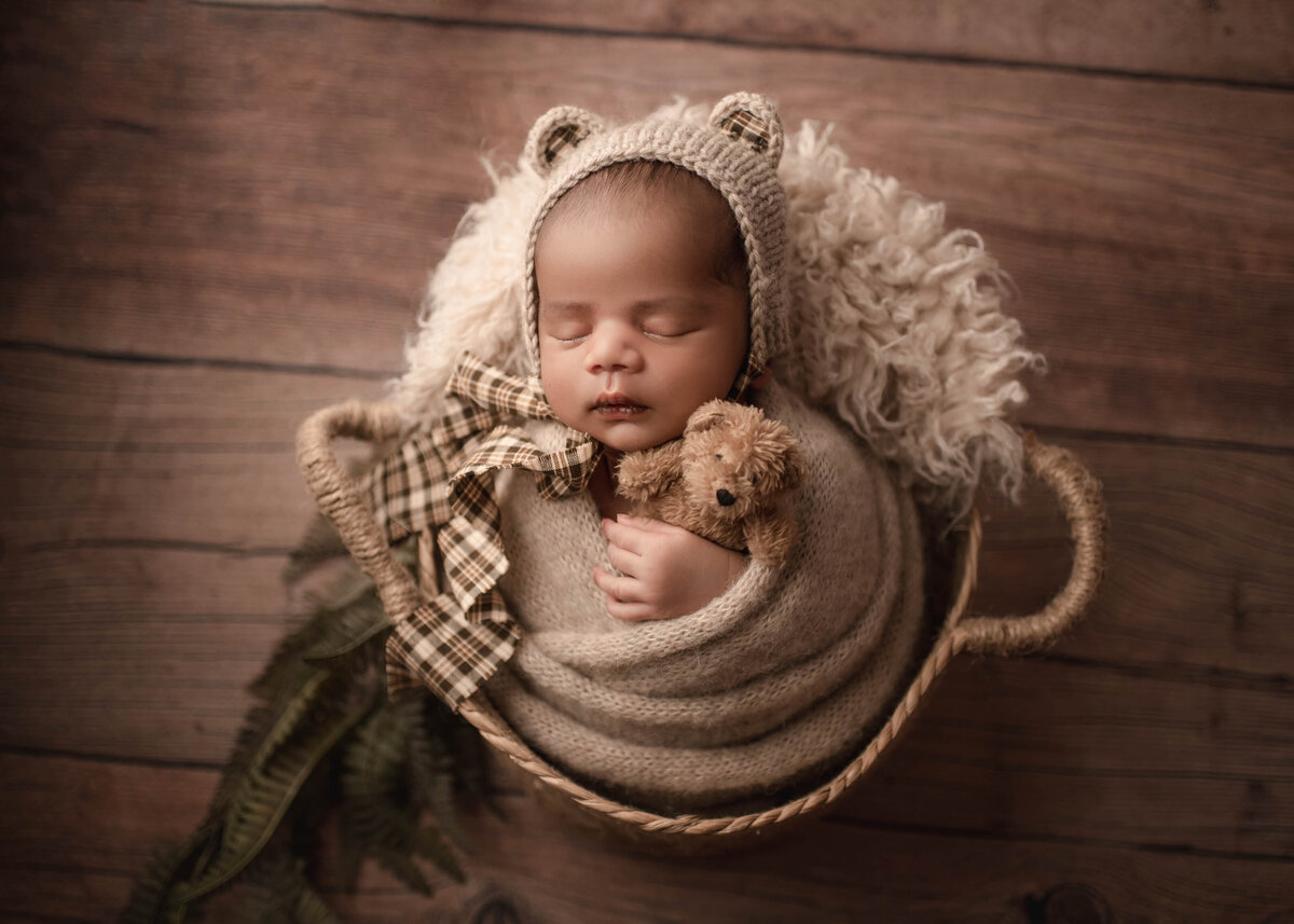 Baby boy wrapped in beige knit posed in basket with bear bonnet