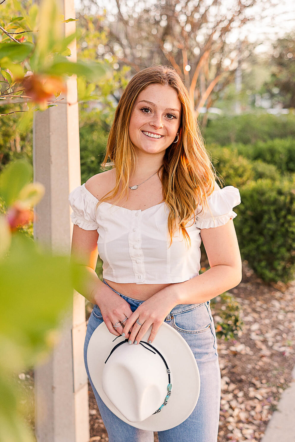 Graduate holding hat near greenery