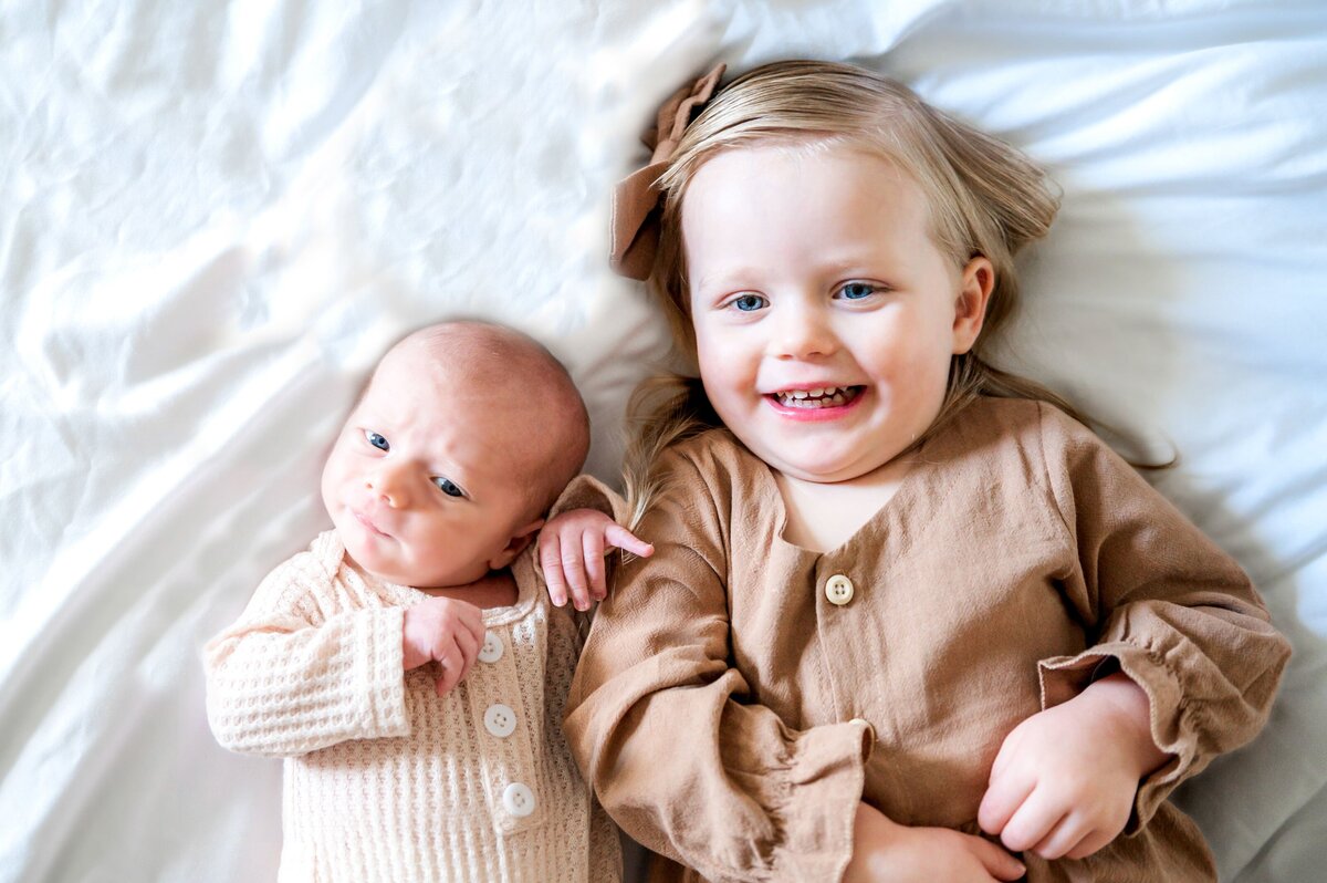 sister in bed laughing with  her newborn brother