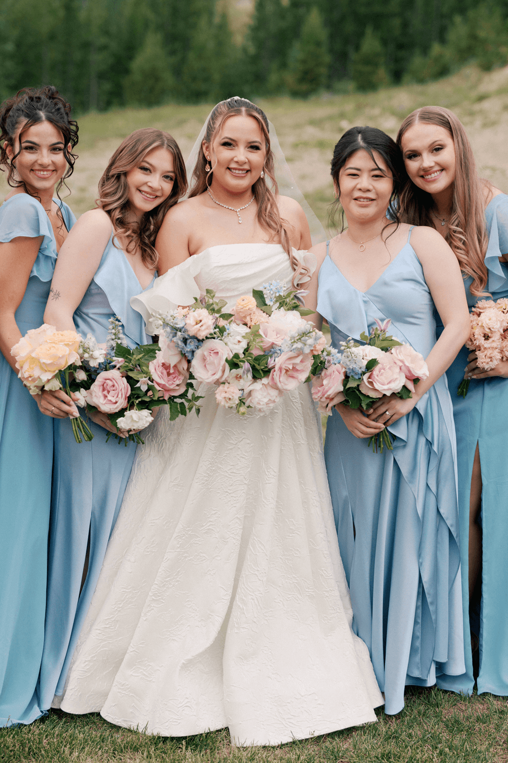 Bride and bridesmaids holding pastel bouquets and wearing soft blue dresses at a summer wedding at Moonlight Basin.