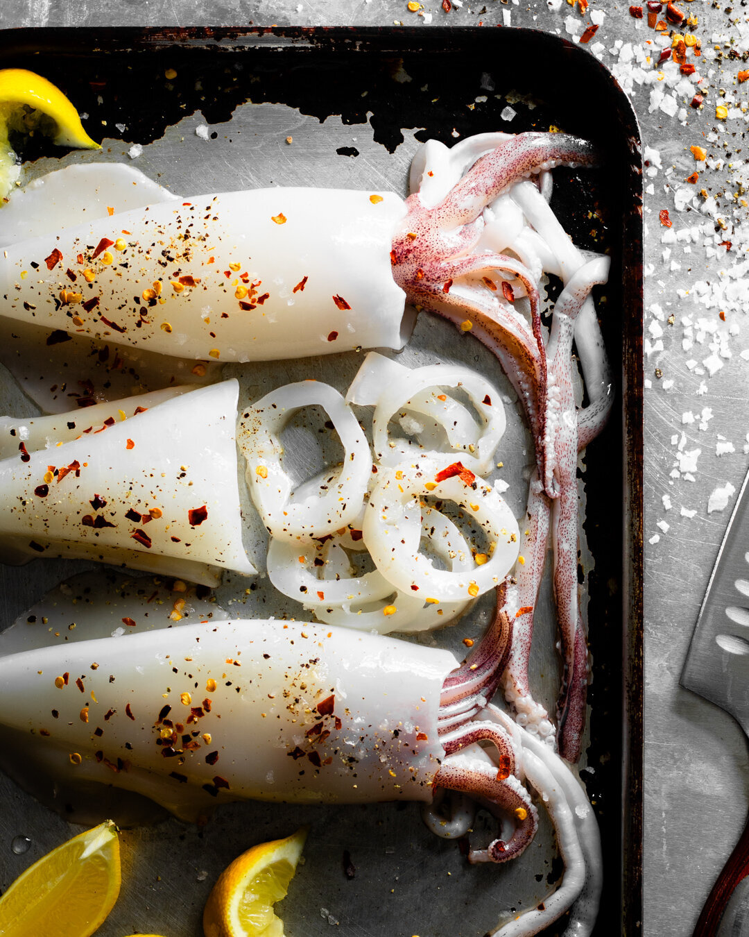 Raw squid on a tray with seasoning and lemon wedges