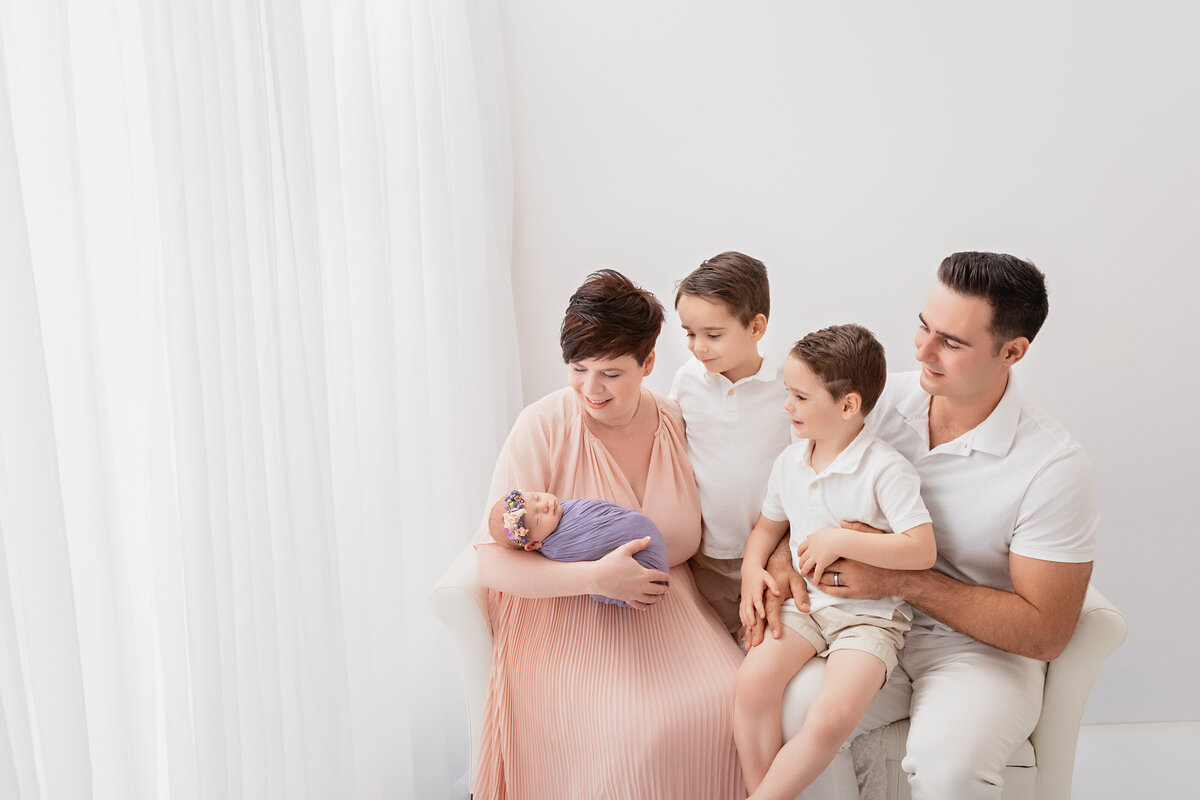 Family holding newborn baby during a soft white studio session