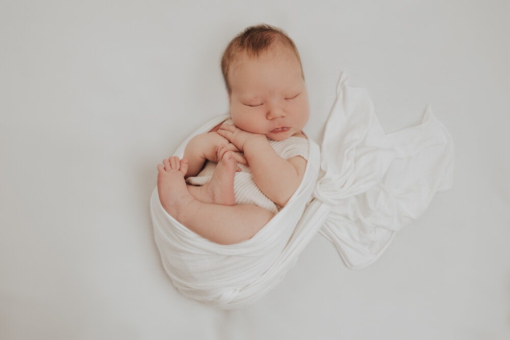 newborn baby wrapped in posing wrap and sleeping on white blanket - Townsville Newborn Photography by Jamie Simmons