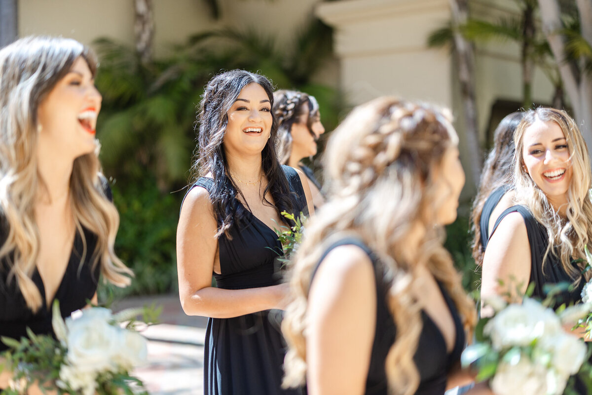 A joyful bridesmaid in a black dress smiles while holding a bouquet, surrounded by the wedding party at Ritz-Carlton Laguna Niguel