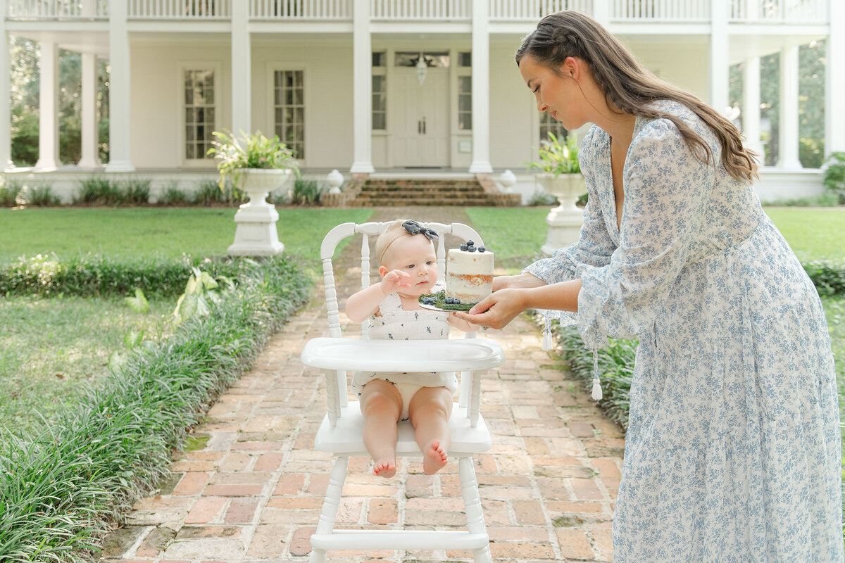 Destin family photographer captures a woman feeding a baby a smash cake in front of a house in a garden.