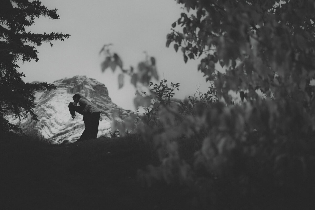 Engaged couple dip and kiss silhouetted against a mountain in Banff