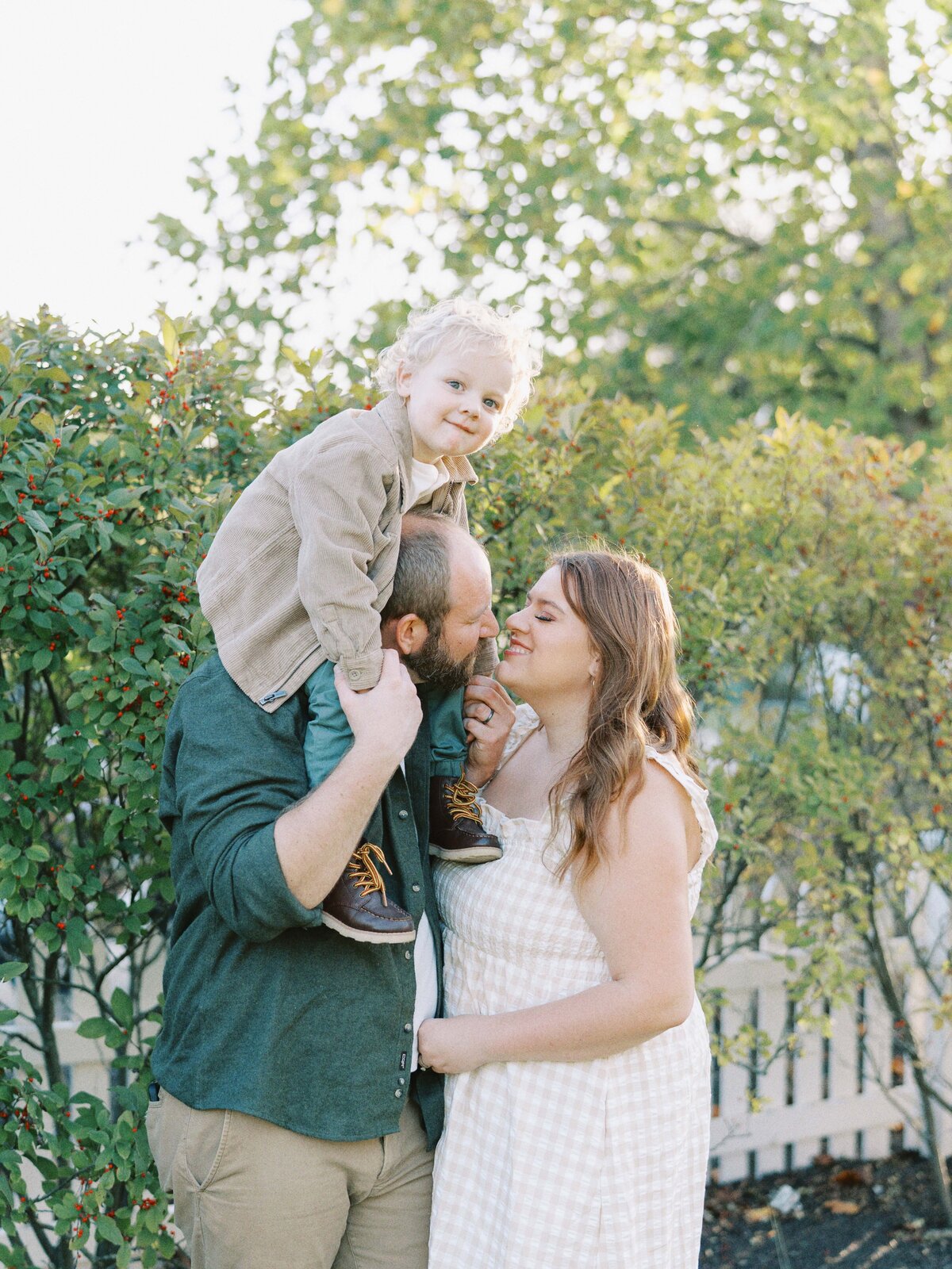 mom and dad kissing with little boy on dad's shoulders