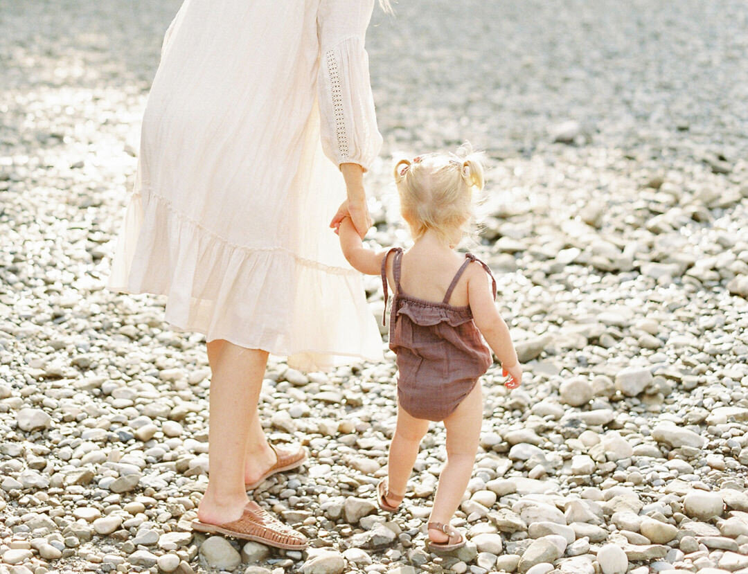 Women holding hands with small child walking over stones