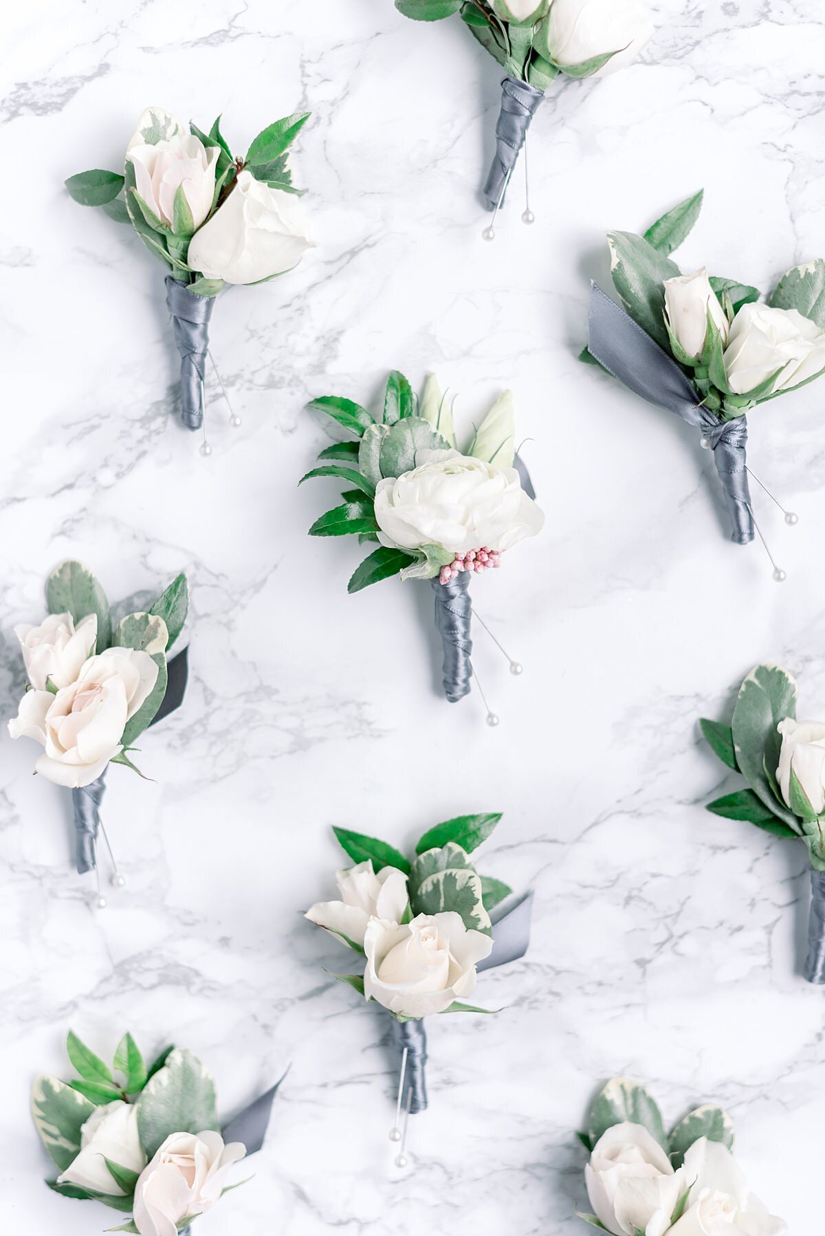 White gardenia boutonnieres with greenery leaves wrapped in silver gray satin ribbon.