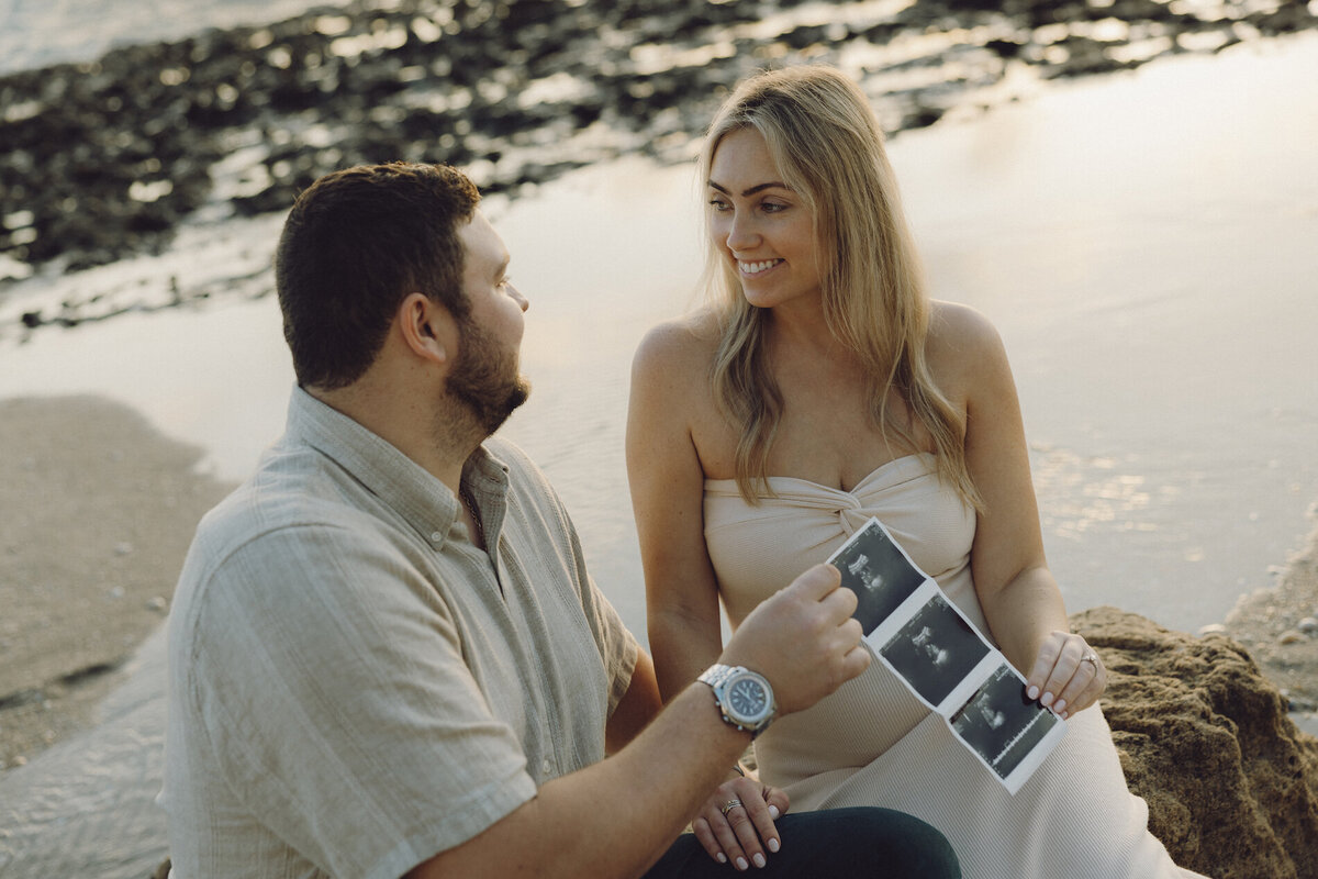 couple holds ultrasound image on beach