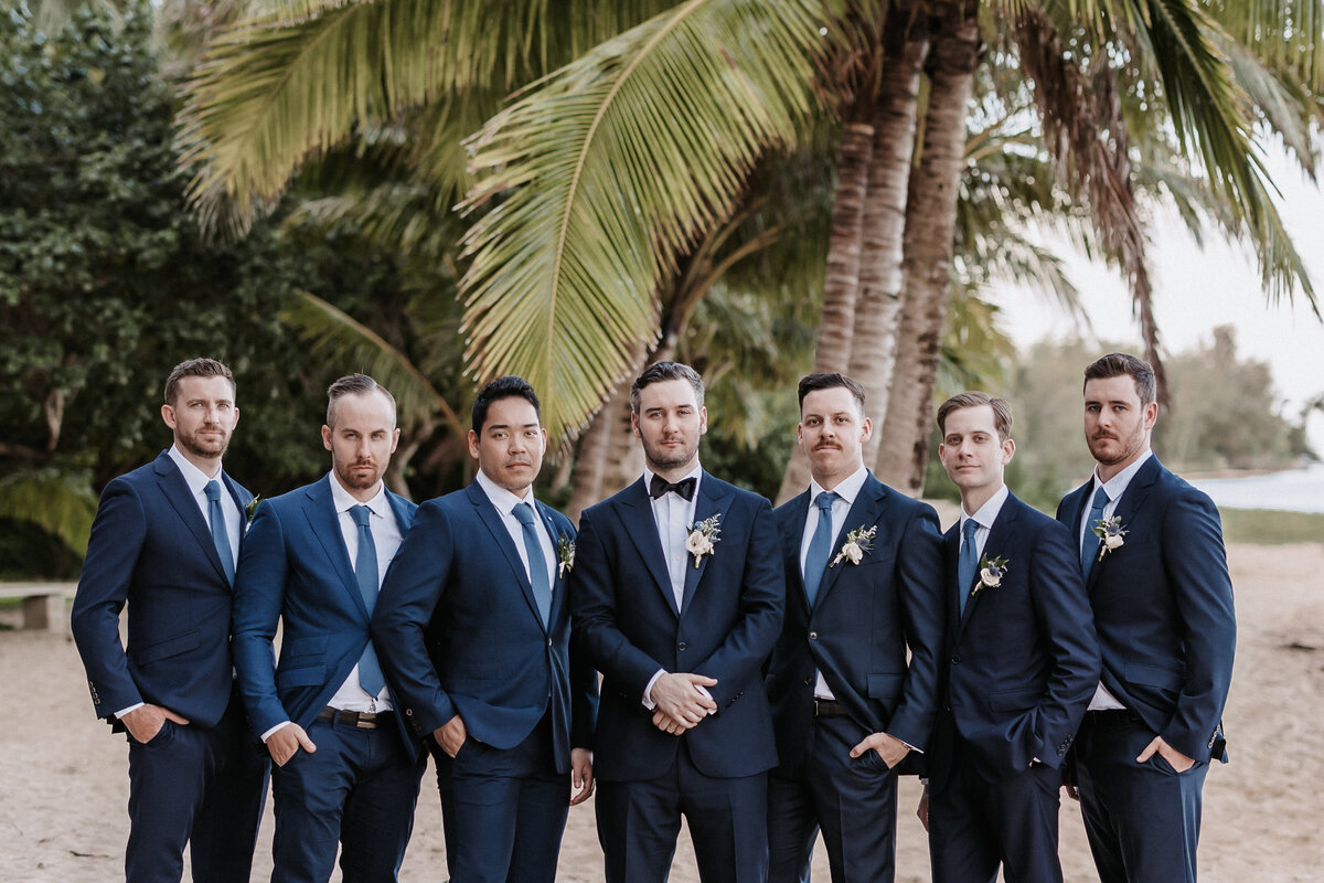 Groomsmen portrait on the beach with palm trees behind wearing navy blue suits