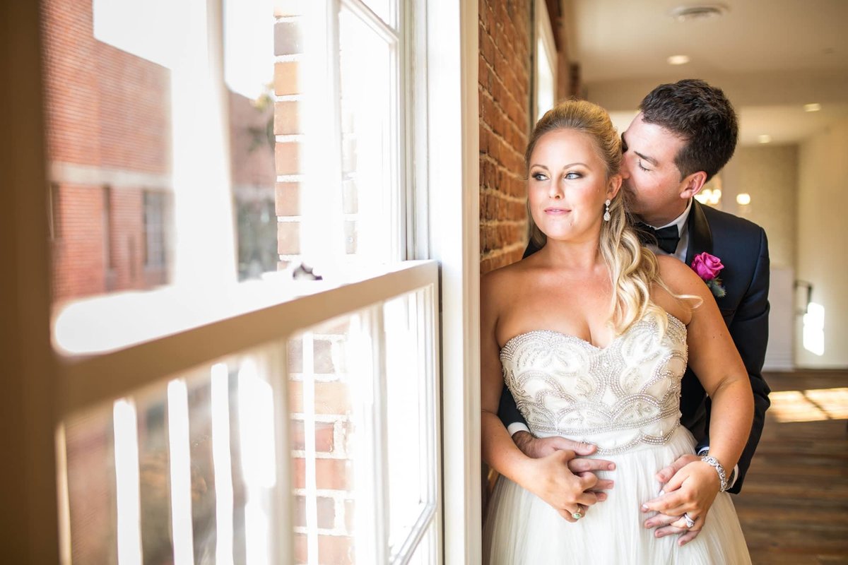 Groom embraces his Bride from behind as she looks out the window