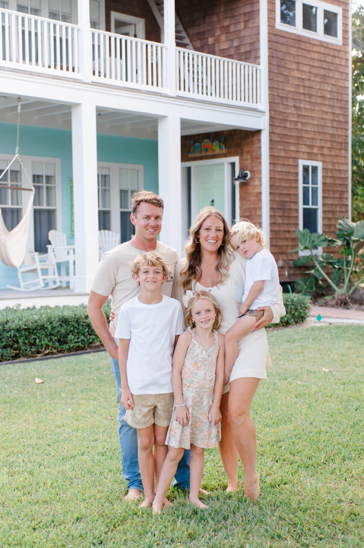 Family stands in front of their Coastal central Florida home smiling at the camera for a family portrait