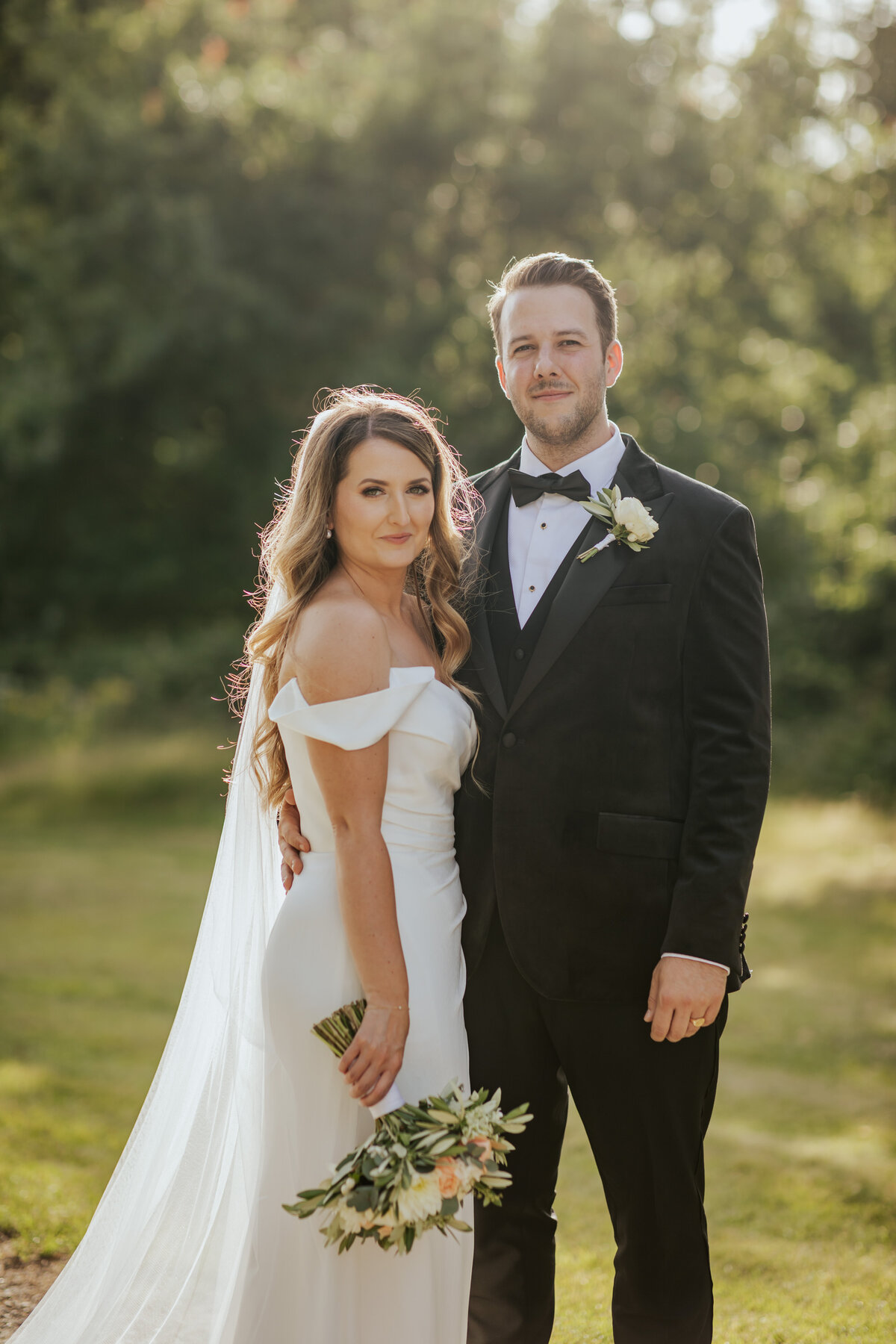 Bride and groom stand posing  with the sun behind them during golden hour at Ufton Court