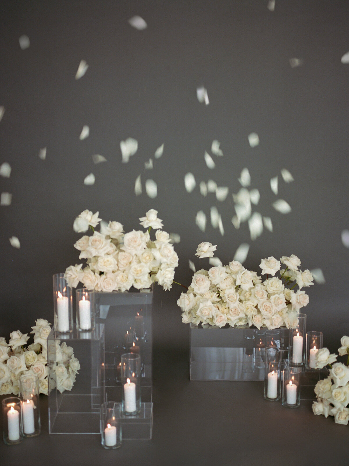 motion of falling white rose petals over scene with abundant white roses, clear pillars, candles, florist film branding photographer