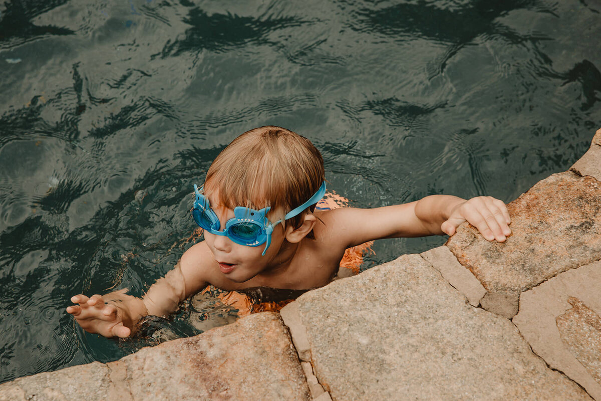 A small child with goggles on holding on to the edge of a pool 