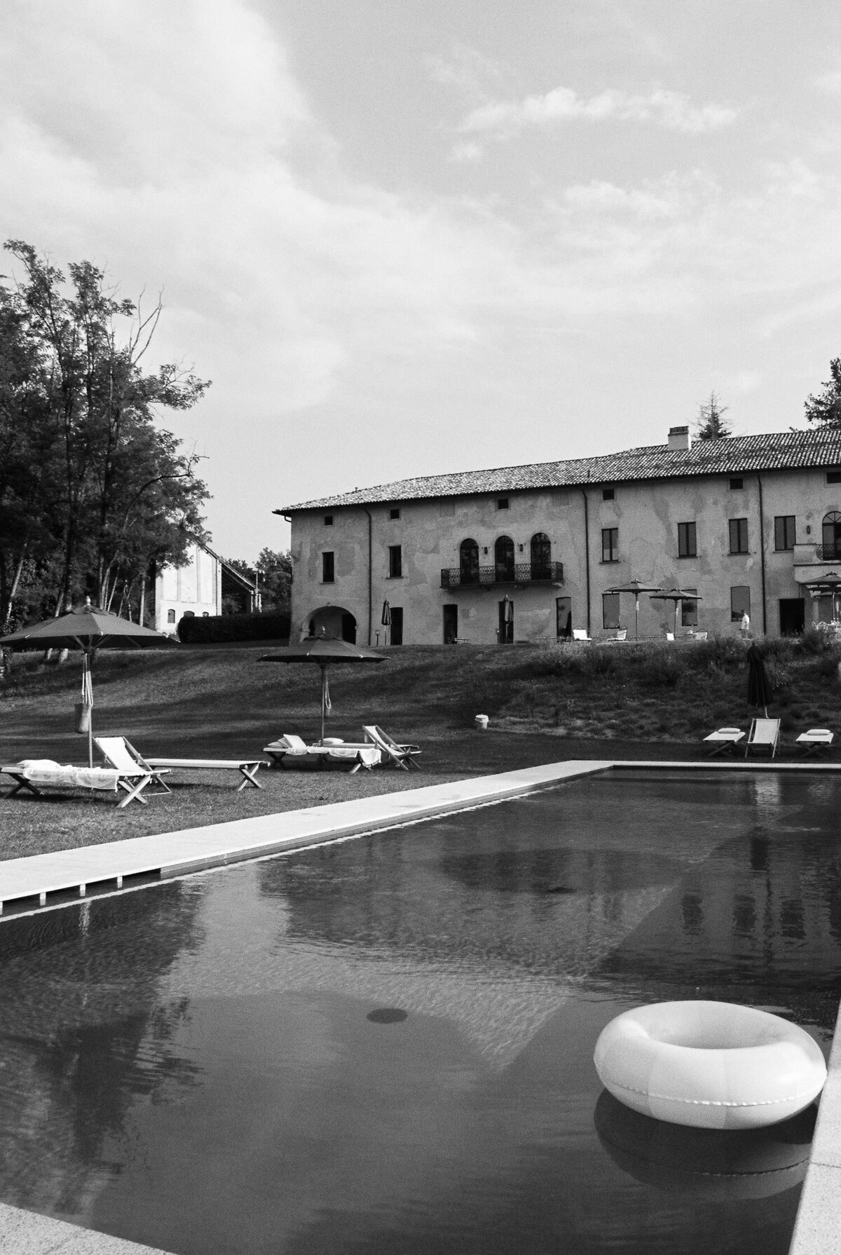 Black and white photograph of Italian villa. Pool with swimming ring in the front and villa in the back. captured by Charleston Film Photographers