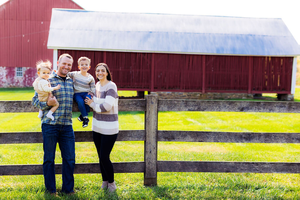 A family of four smiles with farm scenery behind them.