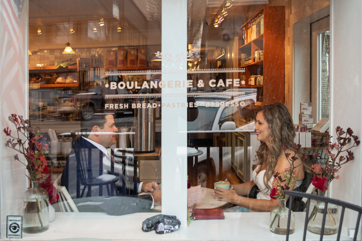 A bride and groom sit inside a coffee shop while their Wyoming elopement photographer takes their photo from outside.