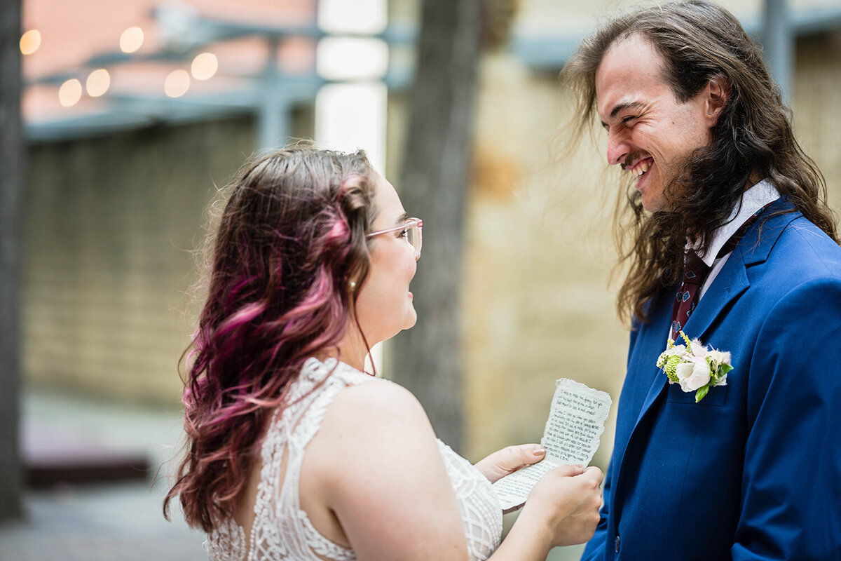 A groom smiles widely at the bride as she reads her vows to him during the ceremony on their elopement day in a tea-light lit alleyway in Downtown Roanoke.