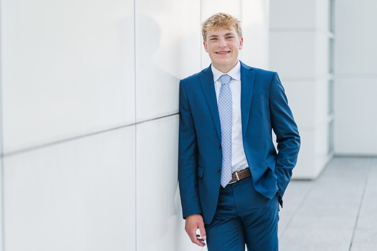 a guy in a blue suit and tie posing against a wall