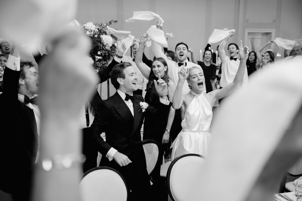 bride and groom celebrating with their bridal party holding napkins in the air