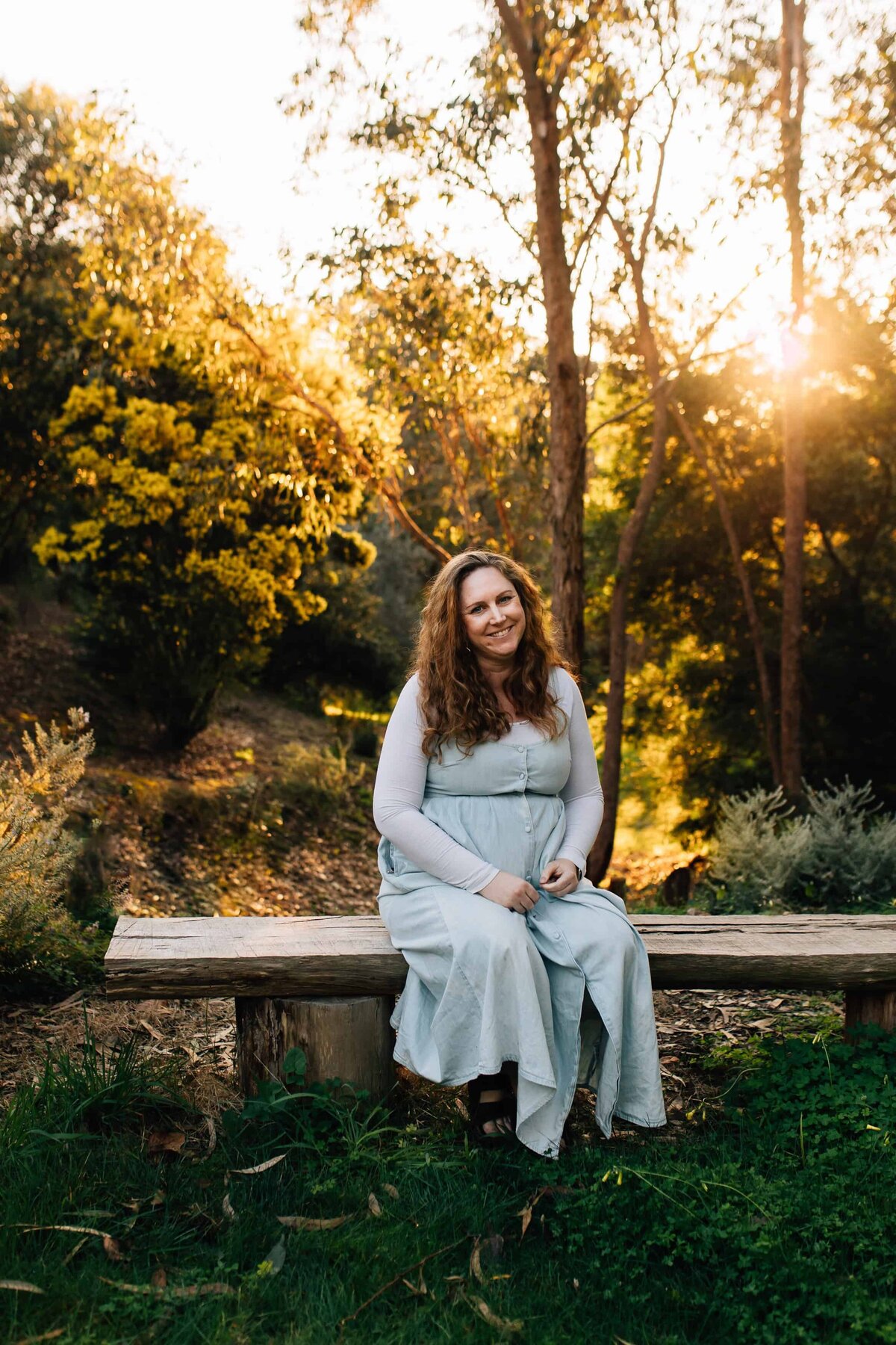 Pregnant woman sitting on bench outdoor with sun setting behind, Melbourne maternity photography.