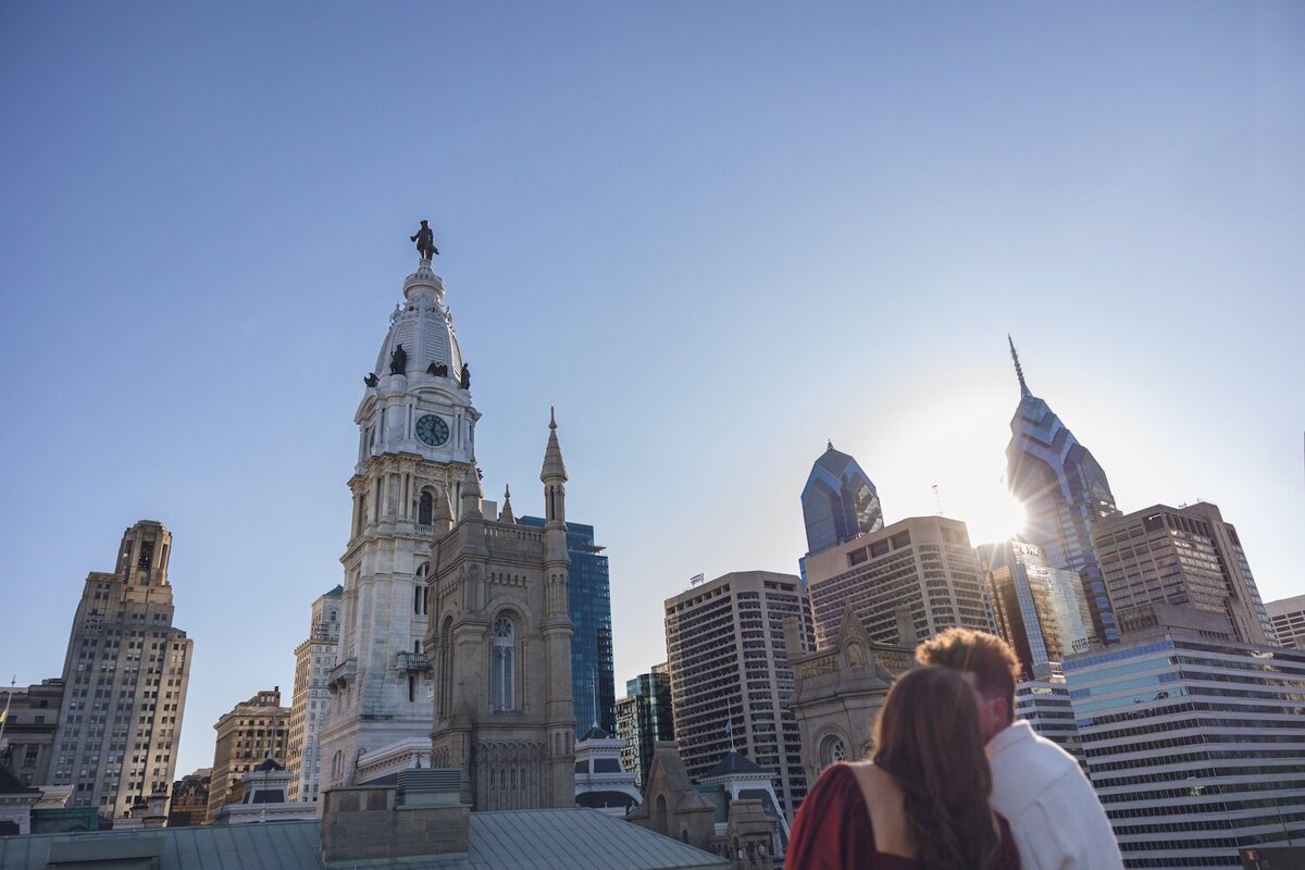 Rooftop sunset kiss framed by historic towers.