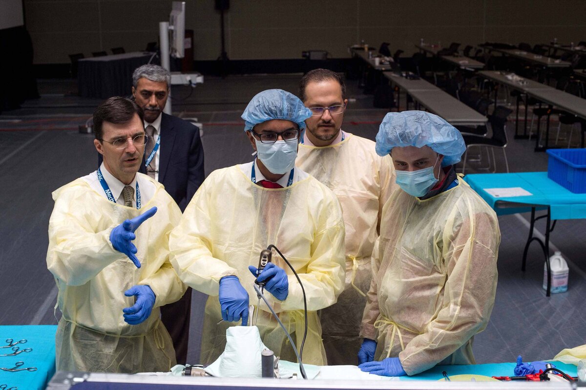 A doctor gestures while another uses handheld surgical tool to practice and neurosurgical technique as others watch during CNS annual meeting