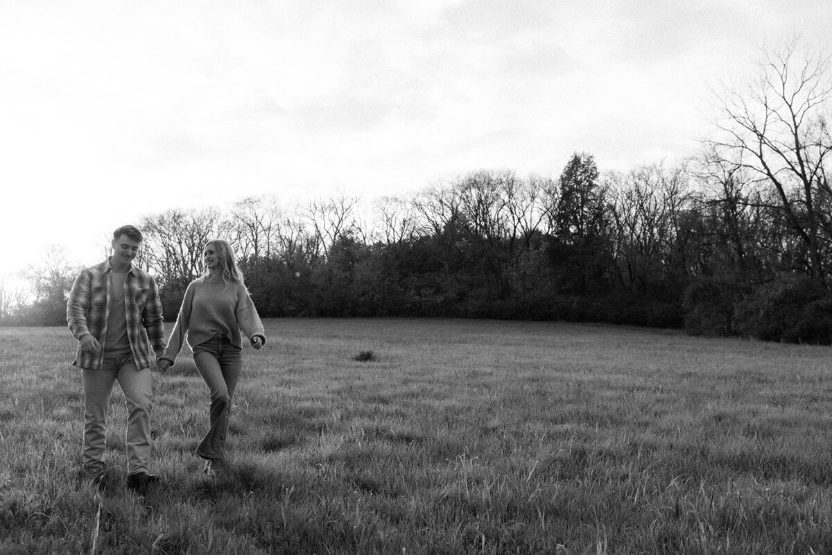 While holding hands, couple walks through the farmland of Franklin, TN during golden hour.