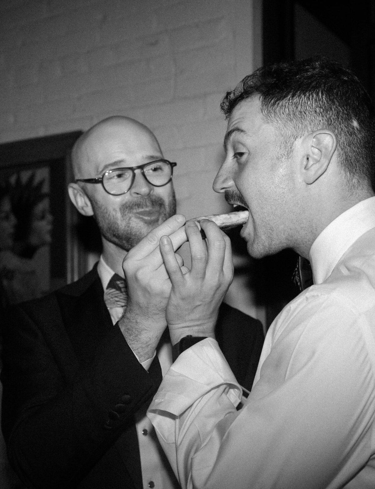 a man feeds his boyfriend pizza at a Detroit wedding afterparty