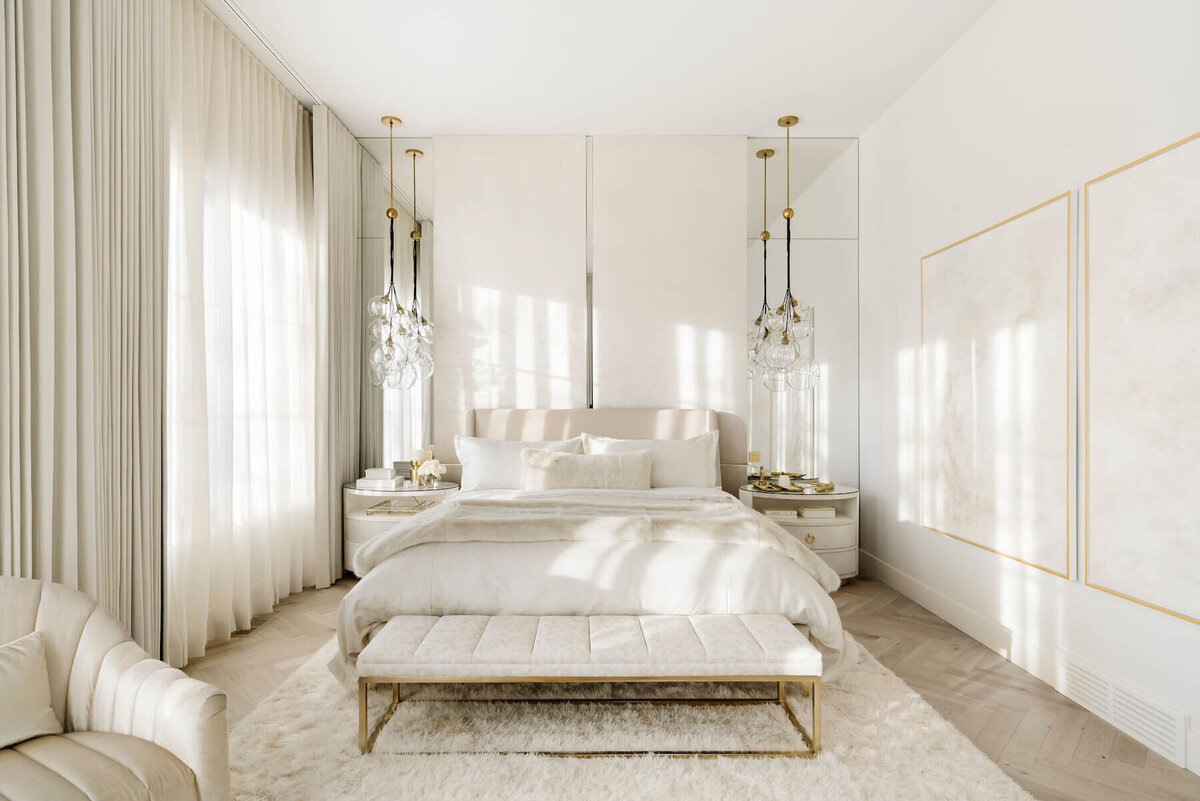 A luxury bedroom with neutral velvet upholstered bed and chairs paired with a textured rug and oversized cluster glass pendants. 