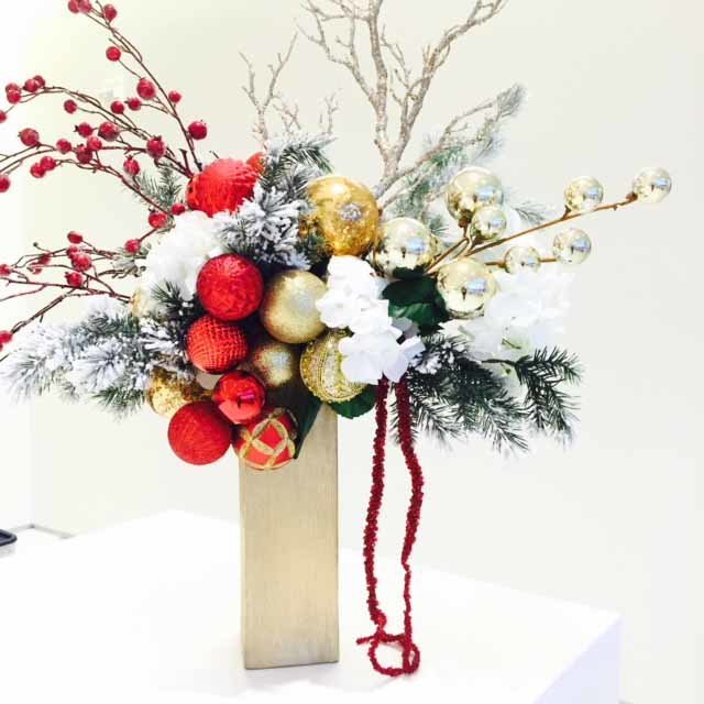 holiday centerpiece with red ornaments, red berry branches, eb=vergreen, white flowers and sparkle branches in  gold vase