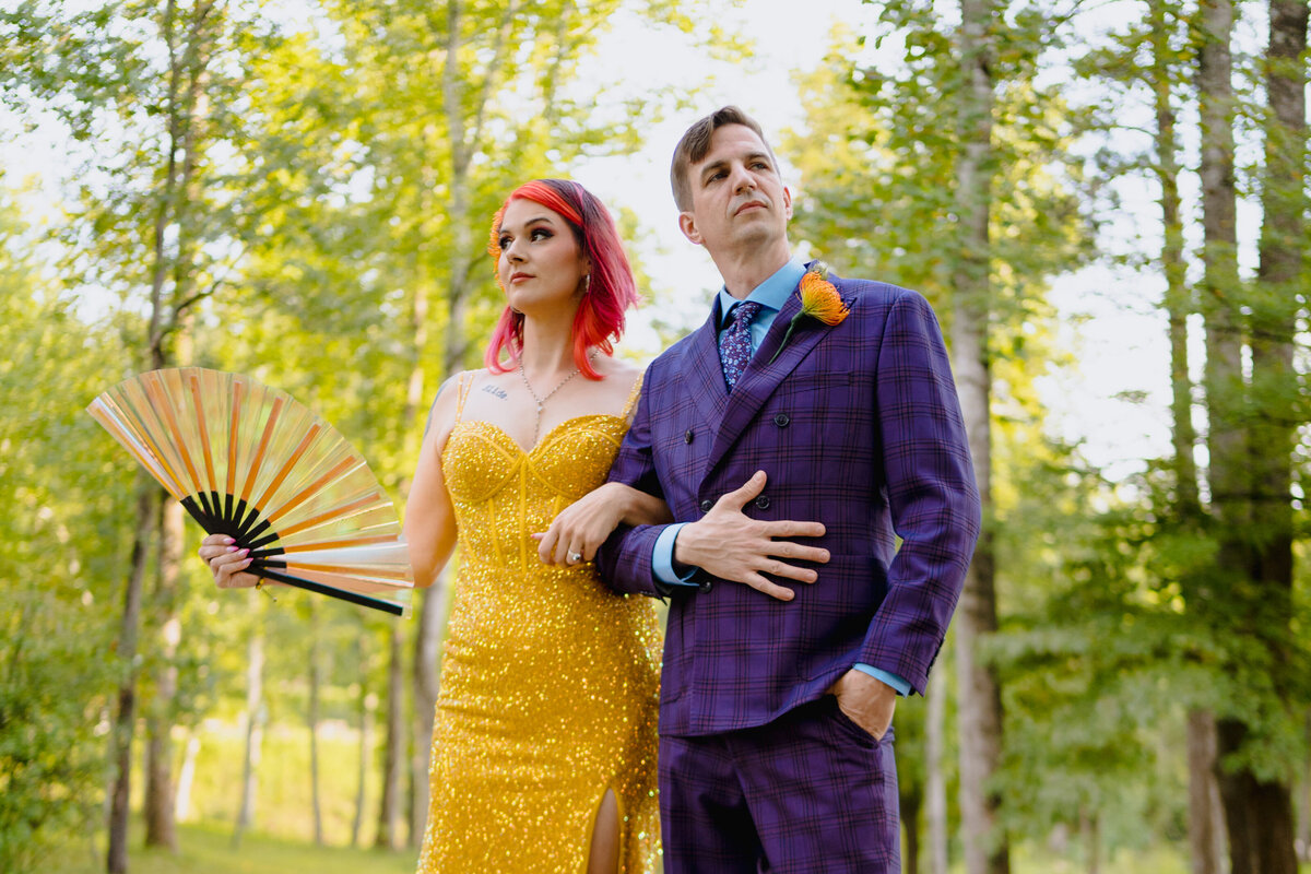 A couple with their arms linked looking opposite directions while one holds a fan.